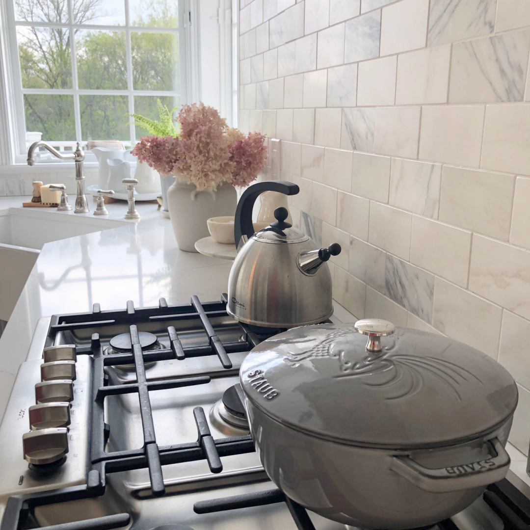 Hello Lovely's light grey and white modern French kitchen with Muse quartz, farm sink, Calacatta marble backsplash and Staub French oven. 