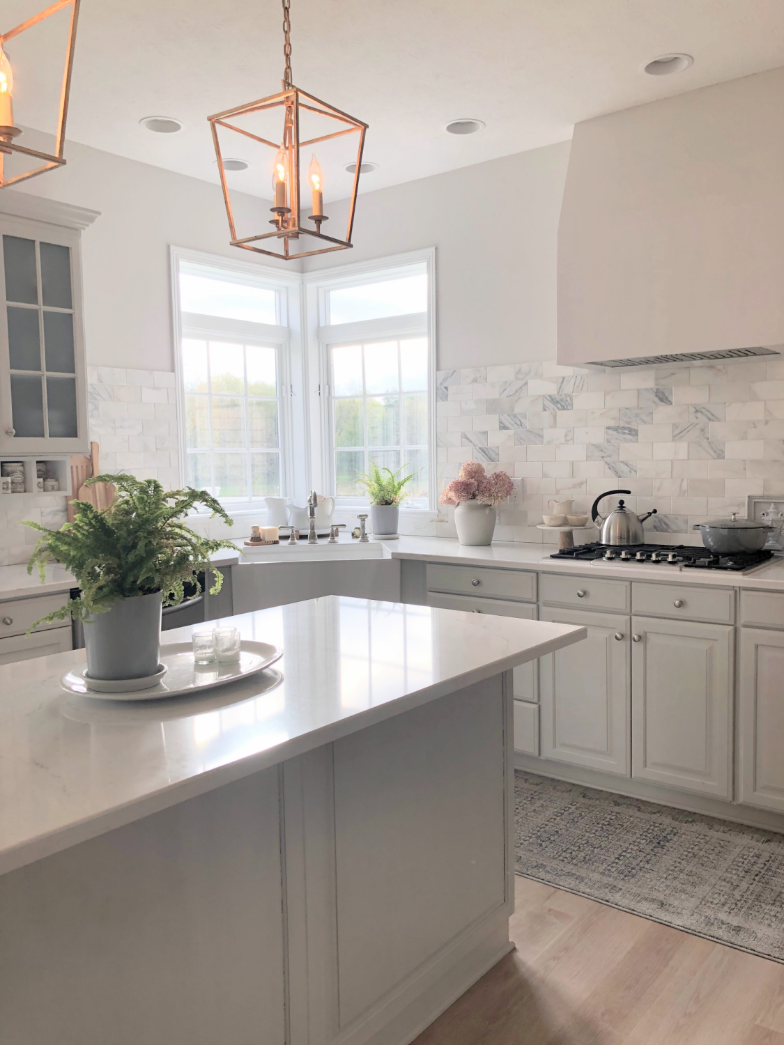 Hello Lovely's light grey and white modern French kitchen with Muse quartz, farm sink, Calacatta marble backsplash, Darlana lanterns, and Staub French oven.
