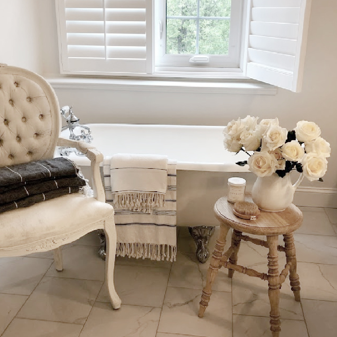 Hello Lovely's white modern French bath with clawfoot tub, Louis chair, country wood stool and white roses. #modernfrench