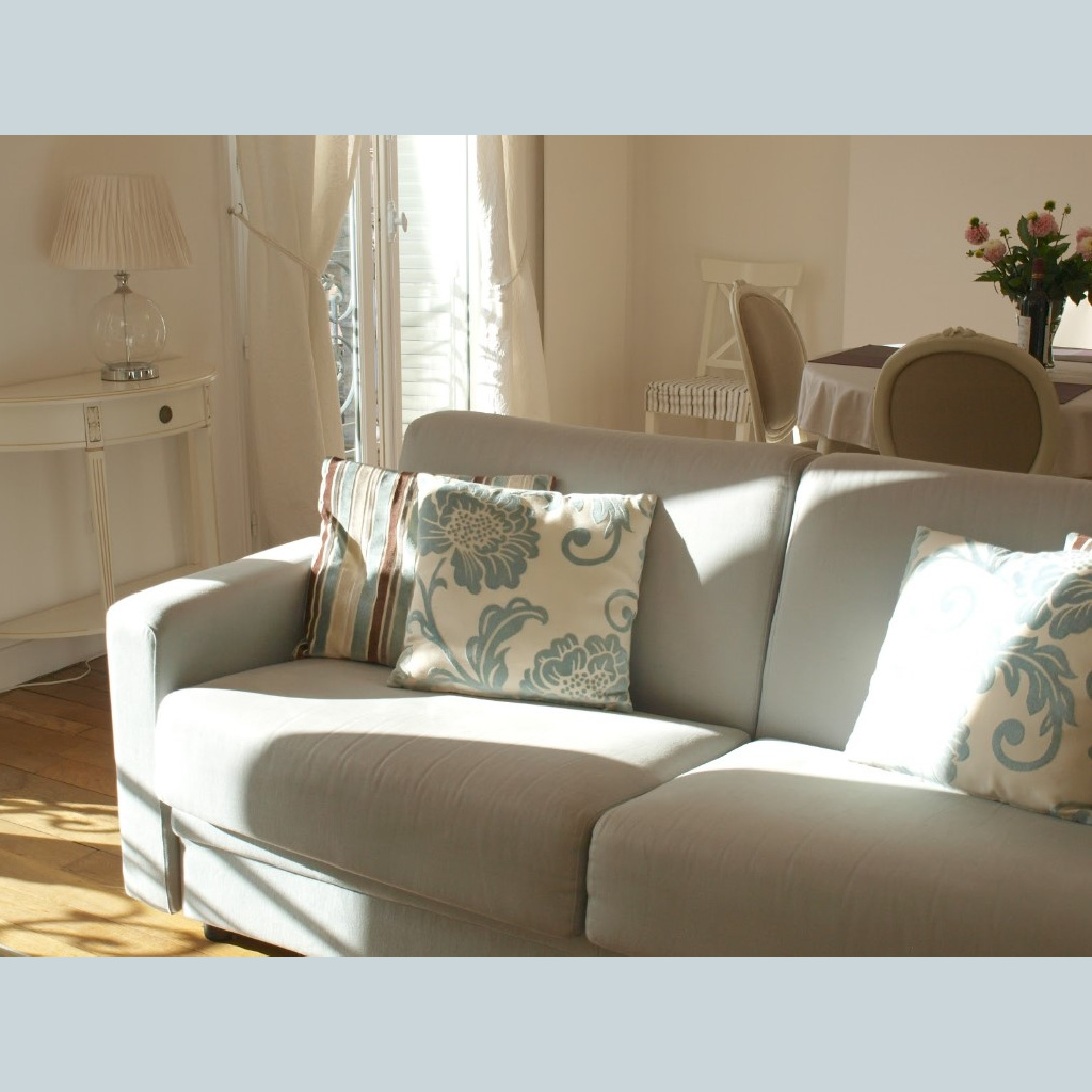 Dappled light on a light blue sofa in a Paris apartment with wood floors - Haven In.