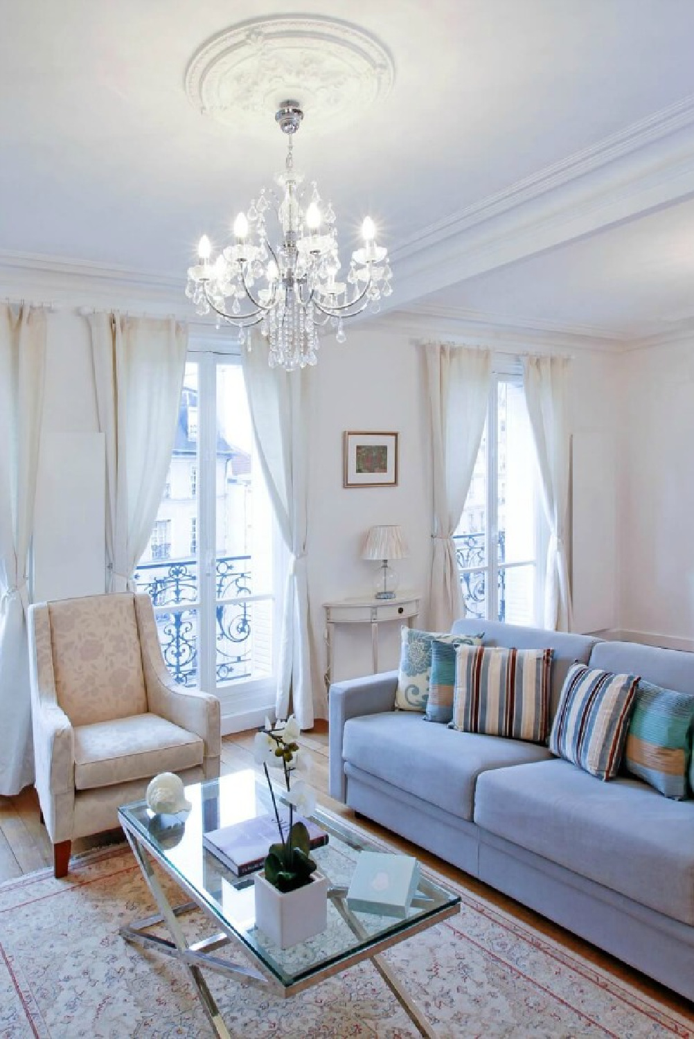 Paris apartment living room with white trim, crystal chandelier, and French doors to balcony - Hello Lovely Studio.