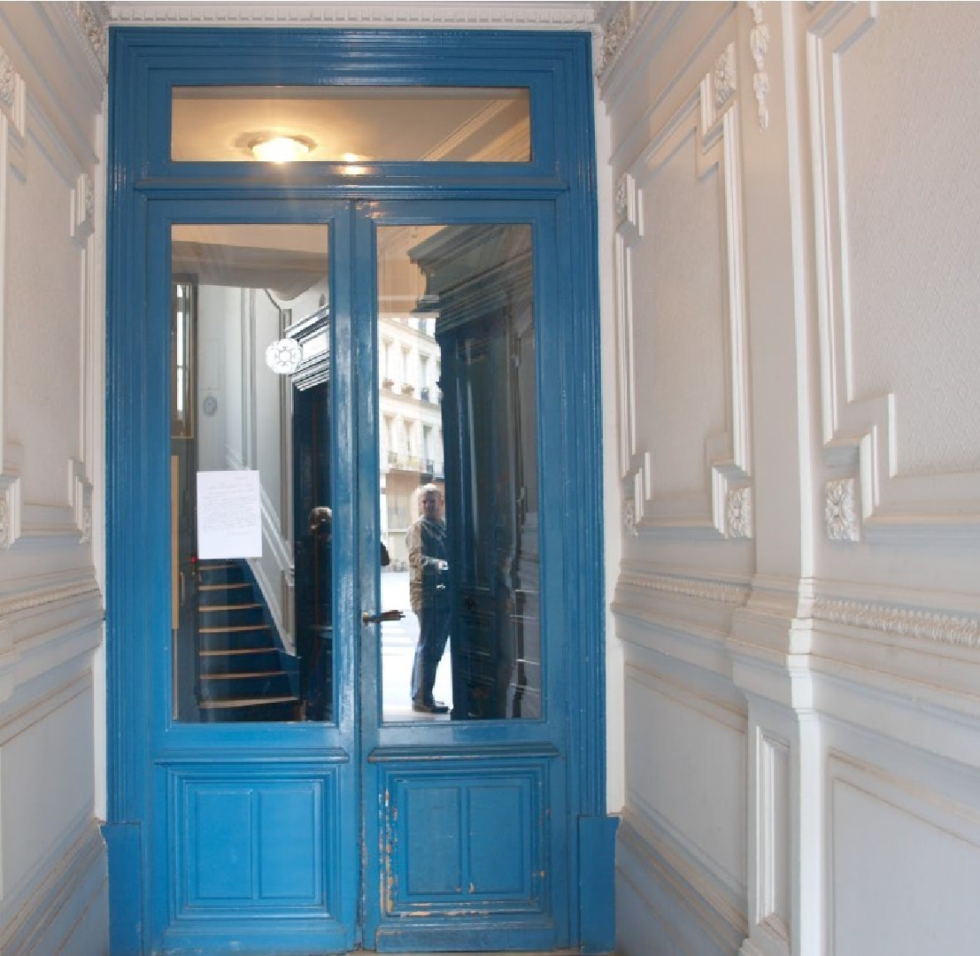 Magnificent paneled white walls and royal blue glossy trim in the entrance of a beautiful Paris apartment building near Notre Dame - Hello Lovely Studio.
