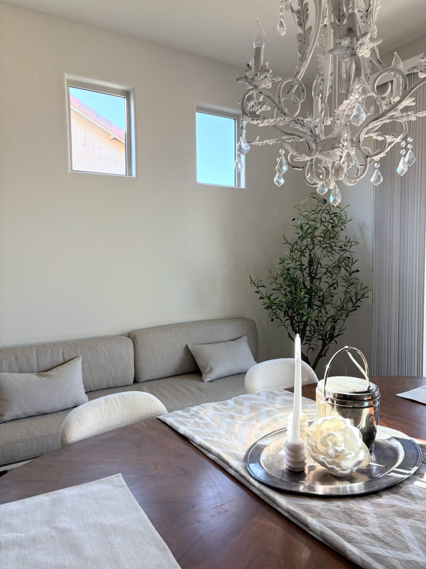 Dining area with a trio of windows above linen cushioned banquette - Hello Lovely Studio.