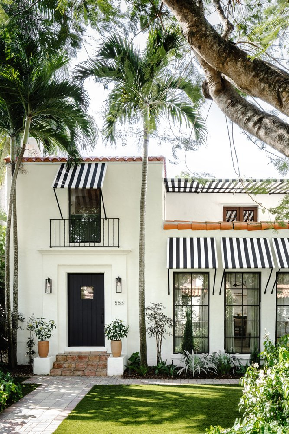 Charming Spanish bungalow facade in Coral Gables with black and white stripe awnings - @calimiahome.