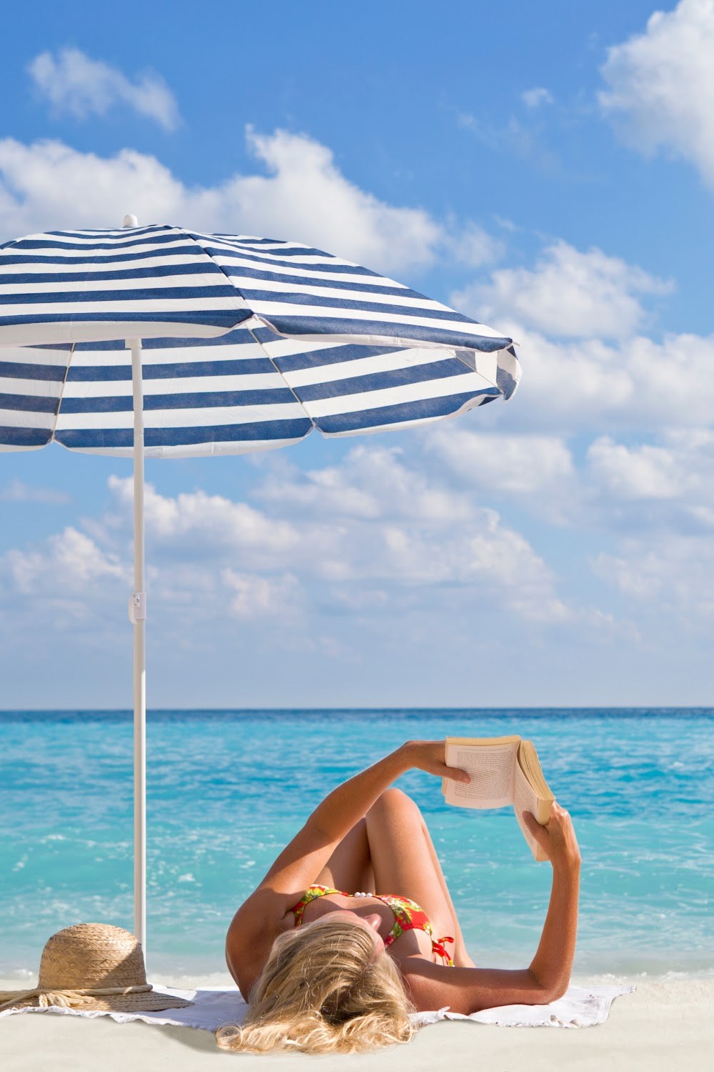 Blonde woman reading on shore at beach with blue stripe umbrella shade canopy and straw hat. #beachumbrella #beachessentials #ad
