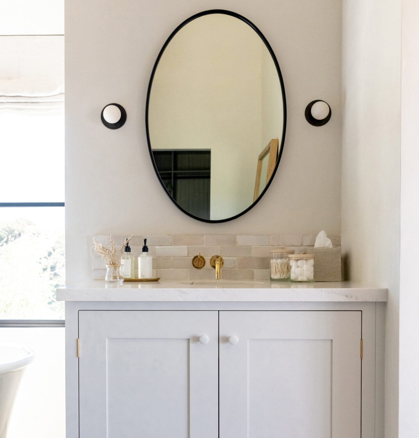 Jenni Kayne Home designed bath with oval mirror and modern sconce lighting.