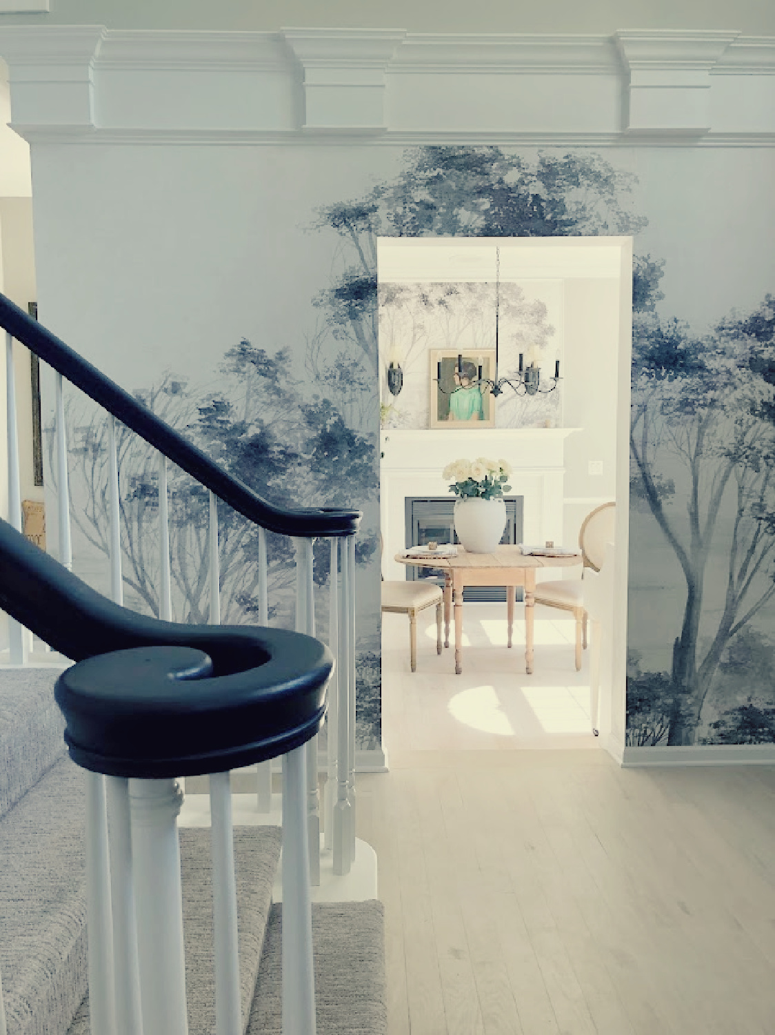 Hello Lovely's entry with grey trees mural wallpaper, bleached oak floors, view into dining room and staircase.