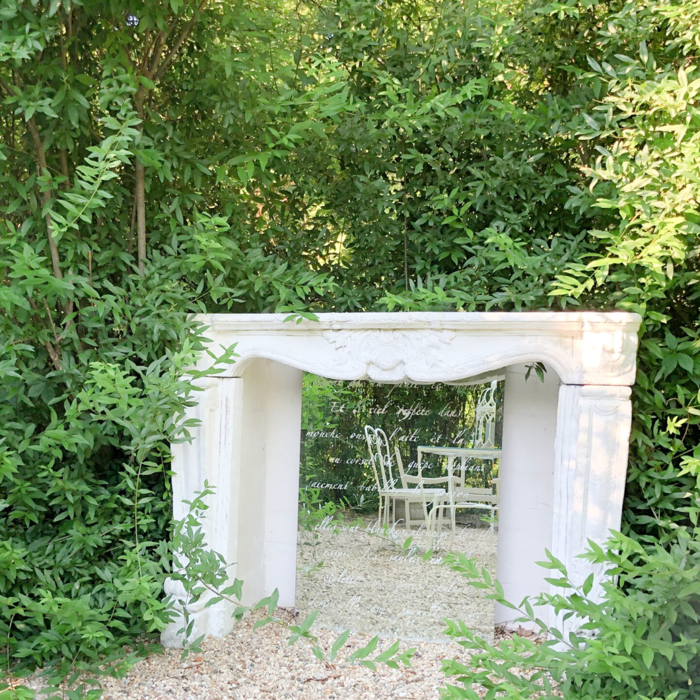 Hello Lovely's French country courtyard is a secret garden hedged with stone fireplace surround and stenciled mirror inside, vintage dining set on pea gravel.