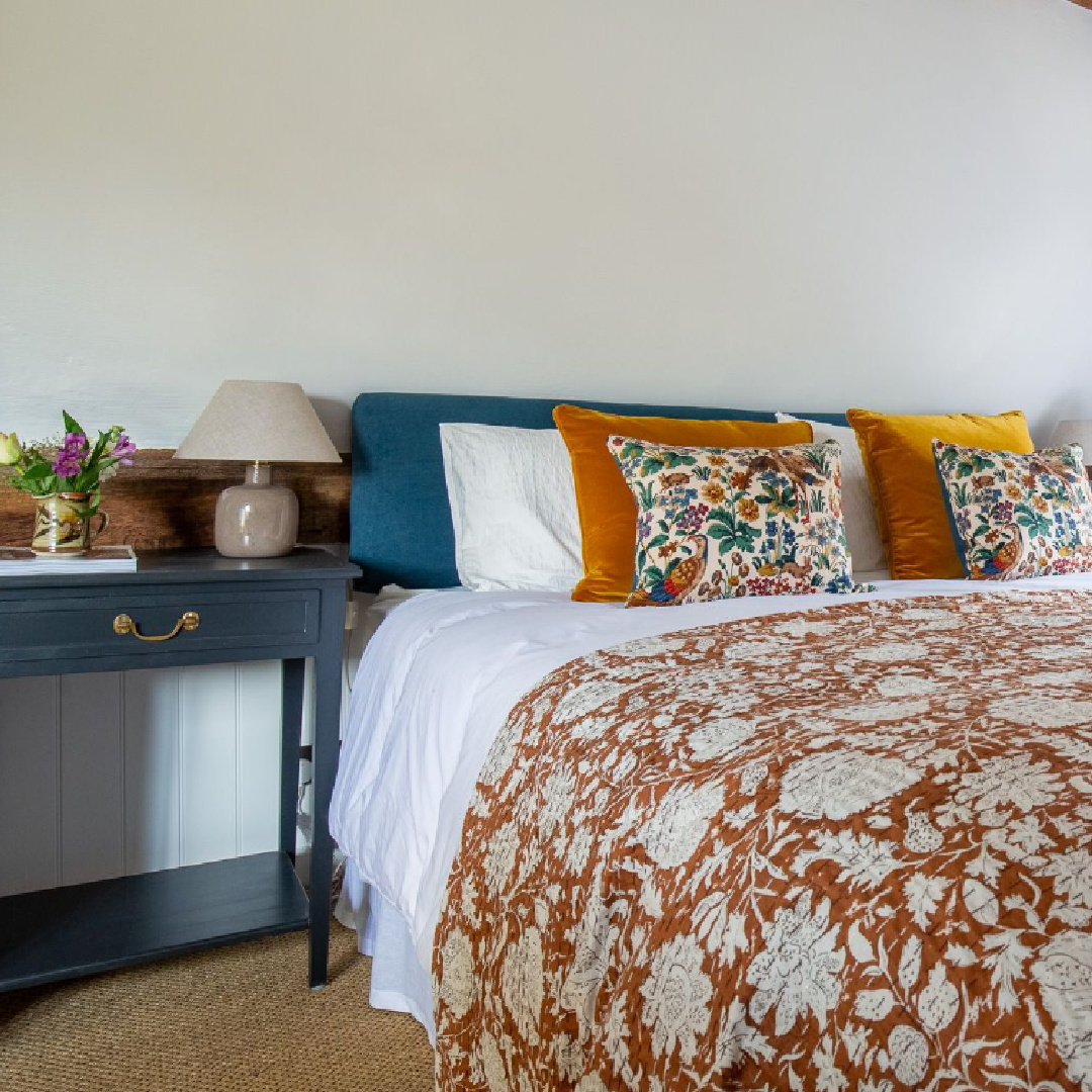 Orange and teal in a bedroom at a Cotswolds stone cottage. Called Armada Cottage dates to 1489 with reimagined interiors by Beth Dadswell (Imperfect Interiors).
