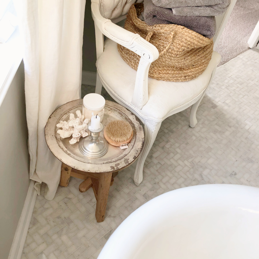 Hello Lovely's renovated bath with herringbone marble mosaic tiled floor and antique chair for holding towels.