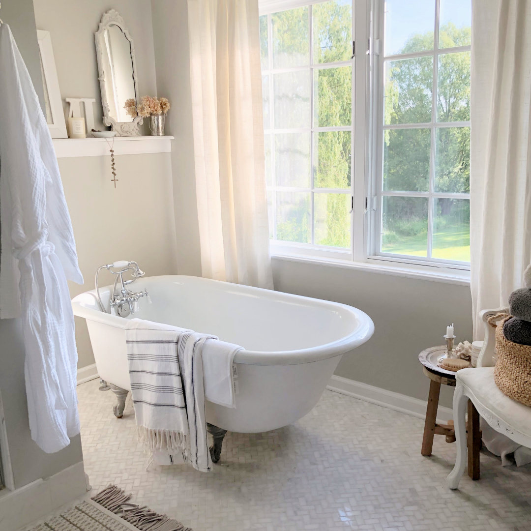 Hello Lovely's serene DIY renovated bath with clawfoot tub, herringbone marble floor, and beautiful view of forest preserve.