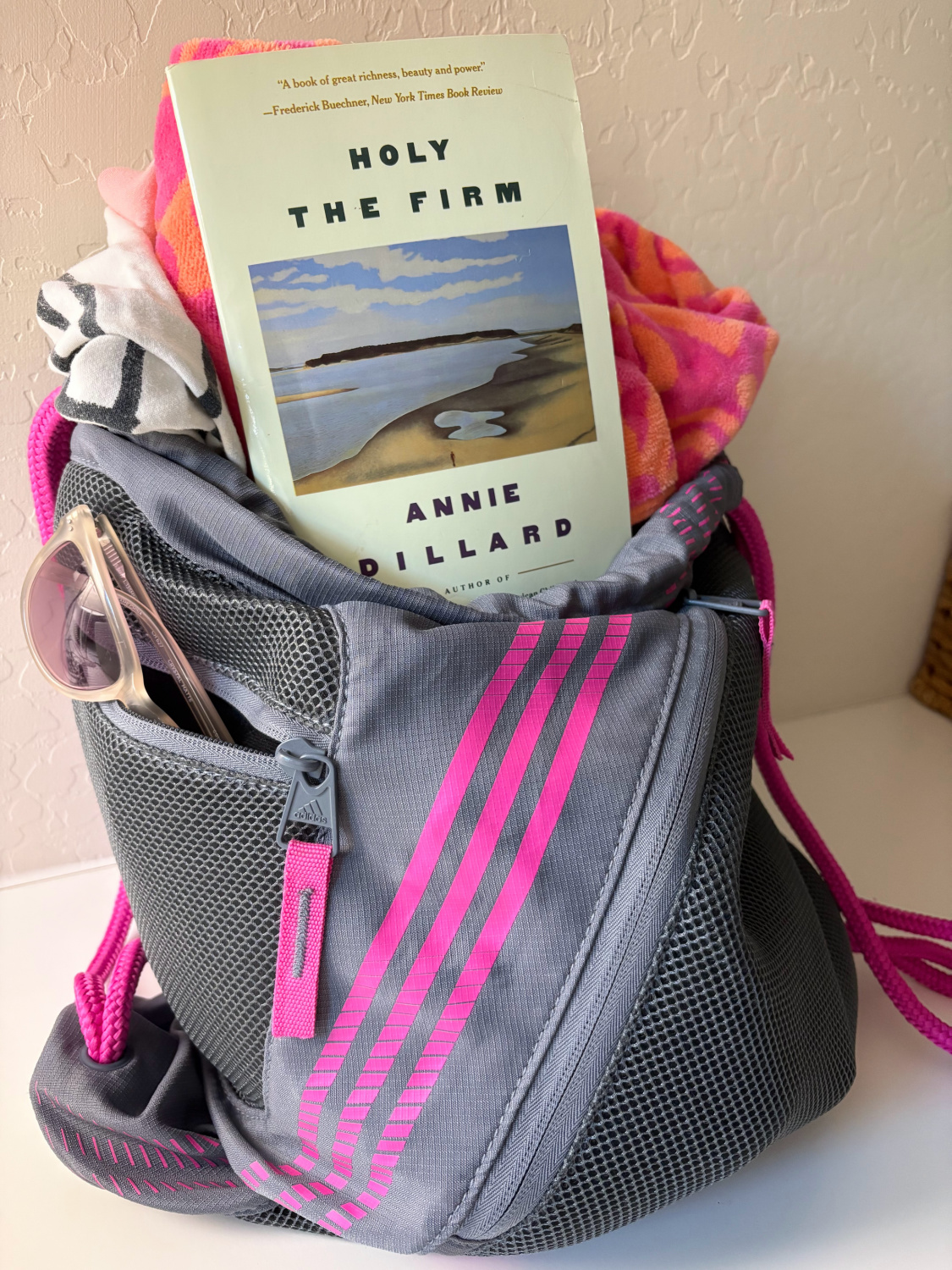 My Adidas sports backpack with beach towel, Annie Dillard's Holy the Firm, and sunglasses - Hello Lovely Studio