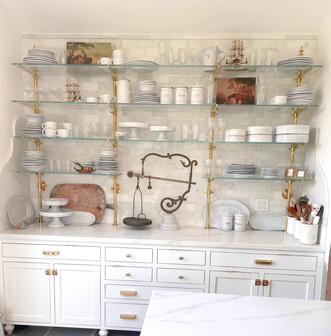 Magnificent French country kitchen with marble, white cabinetry, glass and brass shelving, and serene elegance - Fifi O'Neill.
