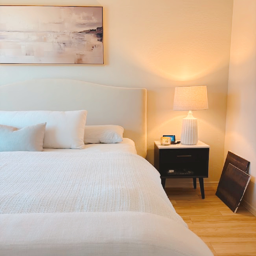 Serene bedroom progress at Hello Lovely's snowbird Arizona retreat. Curved velvet headboard, white linen, black MCM nightstand, and textured lamp.