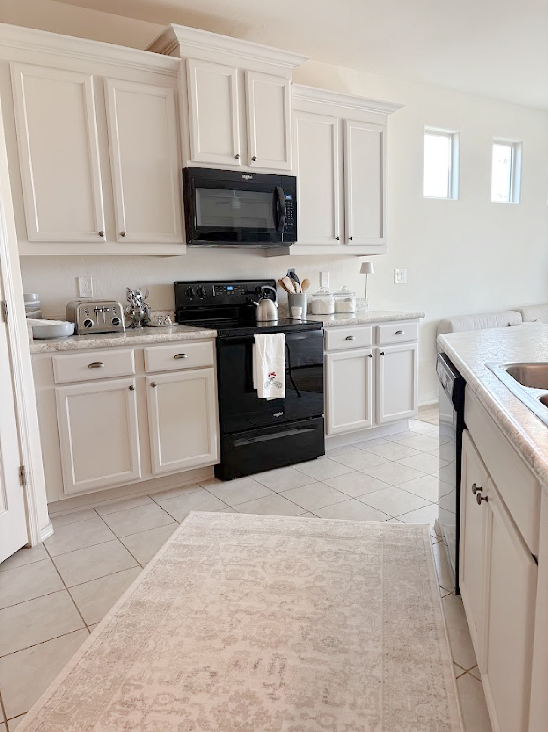 I calmed our Arizona snowbird kitchen cabinets with Sherwin Williams Agreeable Gray, accent lighting, and a pretty rug to cover beige ceramic tile - Hello Lovely Studio.