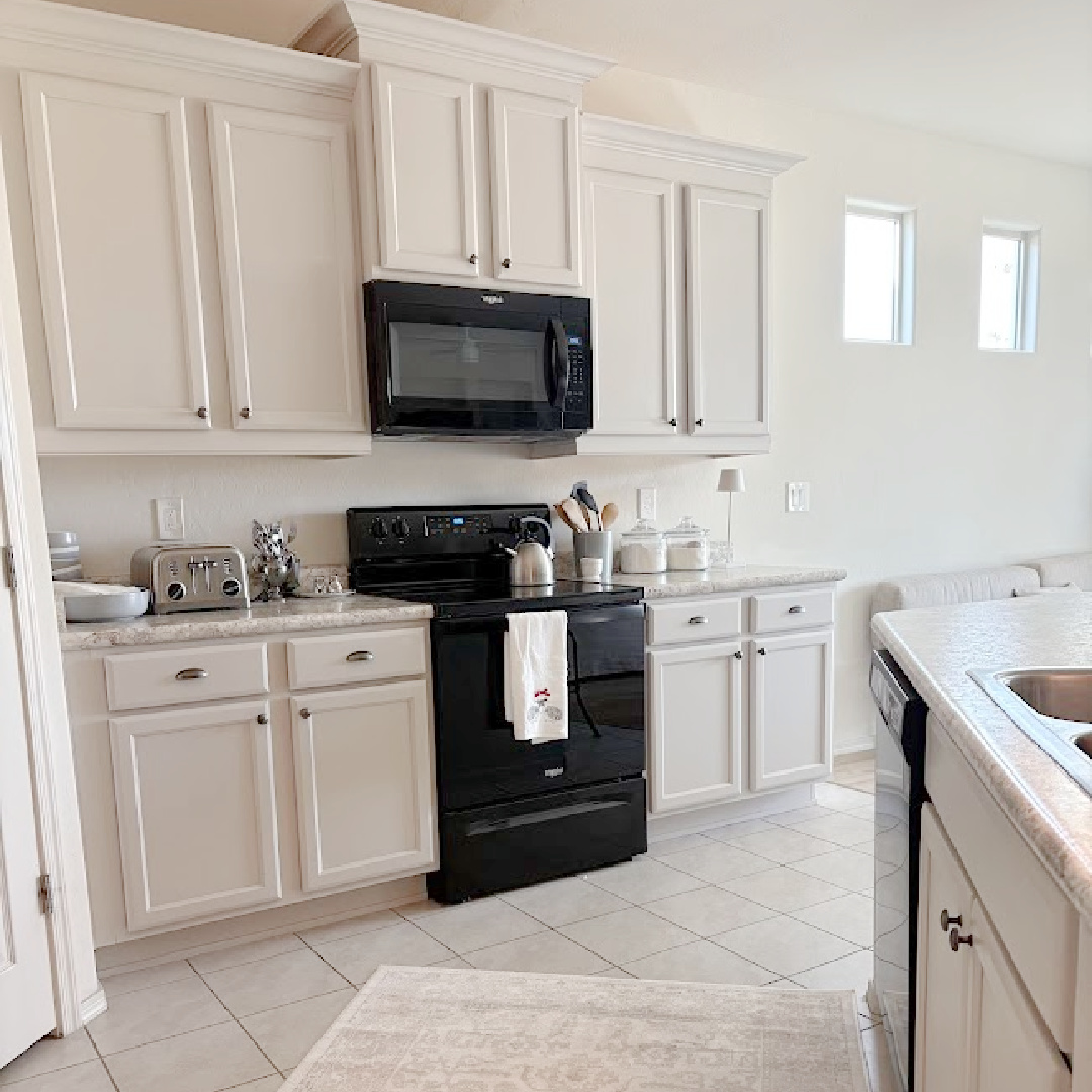 I calmed our Arizona snowbird kitchen cabinets with Sherwin Williams Agreeable Gray, accent lighting, and a pretty rug to cover beige ceramic tile - Hello Lovely Studio.