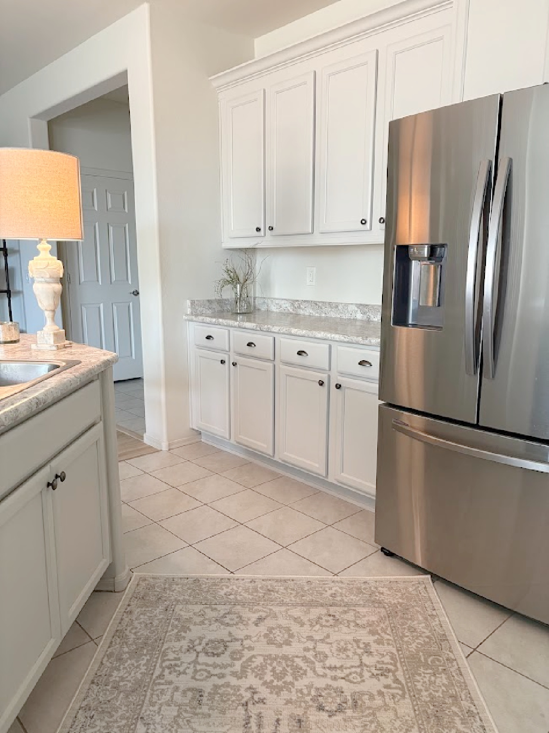 I calmed our Arizona snowbird kitchen cabinets with Sherwin Williams Agreeable Gray, accent lighting, and a pretty rug to cover beige ceramic tile - Hello Lovely Studio.