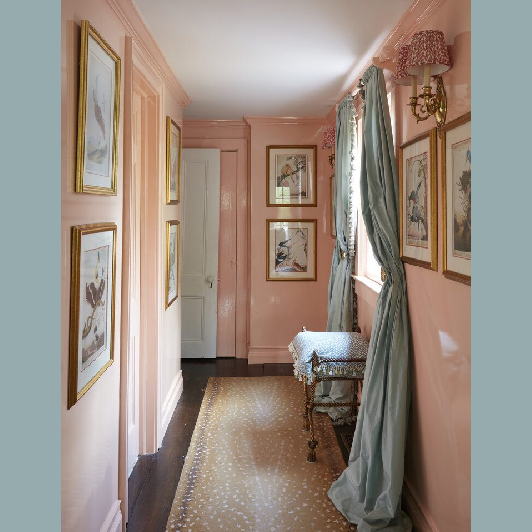 Pretty pink lacquered walls and trim with aqua drapes and classic framed art in a hall with design by Brittany Bromley.