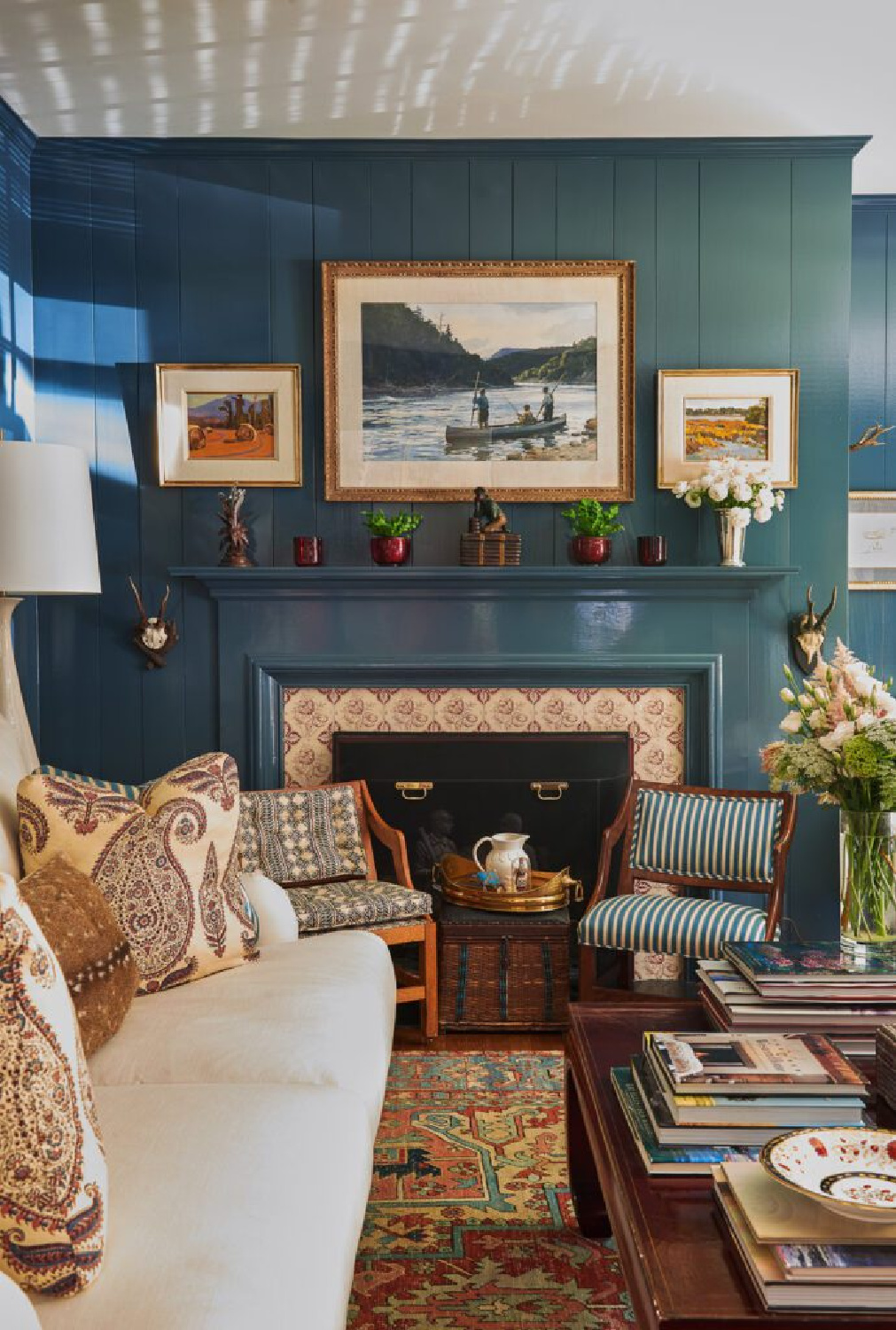 Teal painted paneled living space with coffee table piled with books and fireplace - interior design by Brittany Bromley.