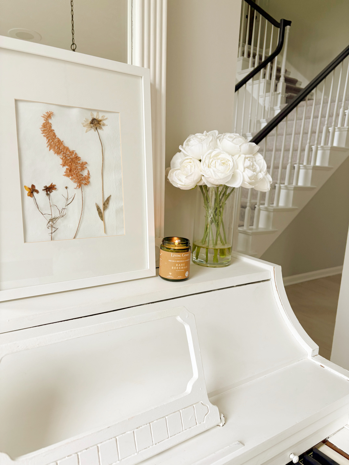Hello Lovely's music room with handmade herbarium and Living Good Candle Co Bare Beeswax candle on white piano.
