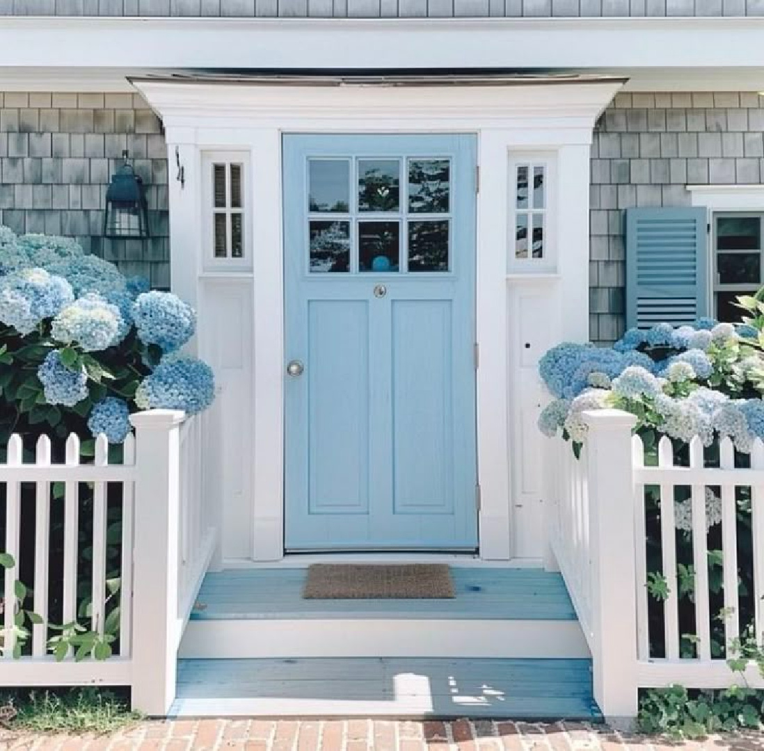 Blue hydrangea blooming on a coastal shingle style cottage with blue door and shutters - via Karen Meijer.