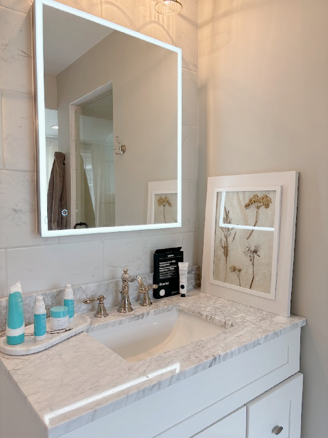 Riversol skincare products (glycolic peel, serum, moisturizer, cleanser) on Hello Lovely's vanity in classic bath with SW Repose Gray walls.