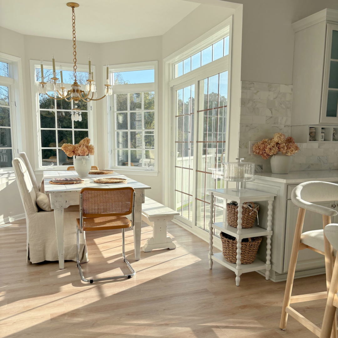 Hello Lovely's modern French kitchen in October with light streaming in turret windows, the breakfast nook with harvest table, linen arm chairs, and Cesca chairs.